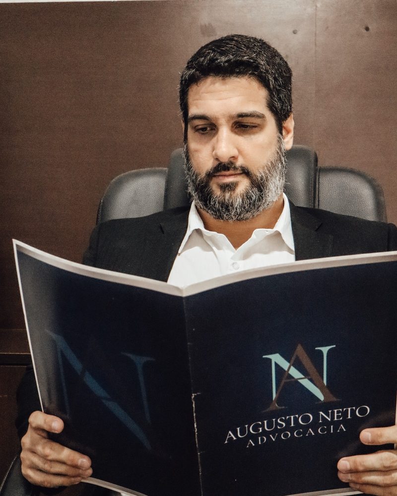 O advogado Augusto Neto, de terno, lendo uma pasta de documentos com o monograma da Augusto Neto Advocacia